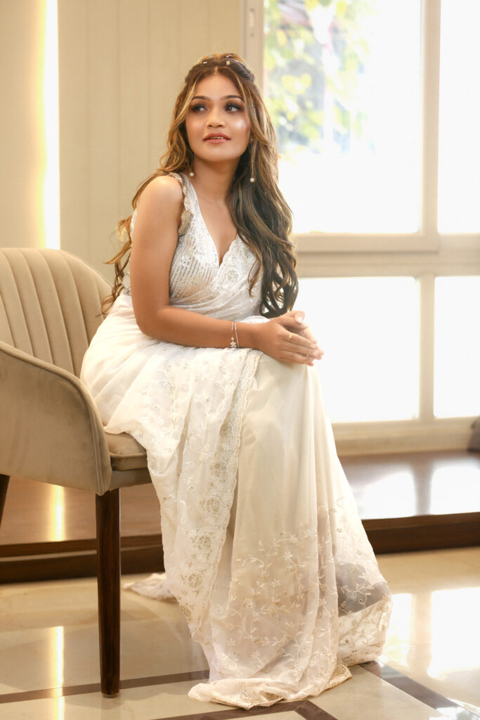 South Indian bride sitting gracefully in a white saree, with soft curls and a radiant reception look in natural lighting.